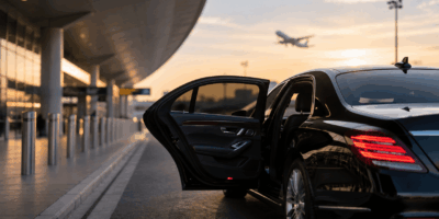 Black luxury sedan waiting outside an airport terminal, representing completed bookings used to calculate limo marketing ROI.